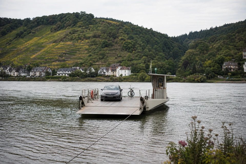 Kleine Autofähre bei der Überfahrt über einen breiten Fluss, ein Pkw und ein Fahrrad an Bord (mit AI erstelltes Bild)