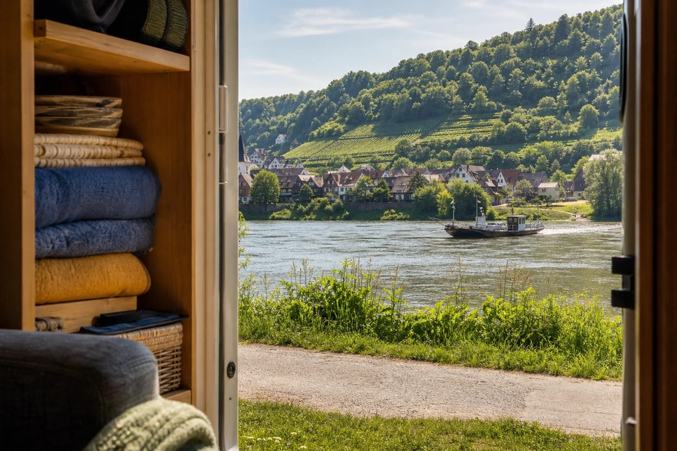 Offene Wohnmobiltür mit ordentlich gepackten Regalen und gefalteten Decken im Morgenlicht (mit AI erstelltes Bild)
