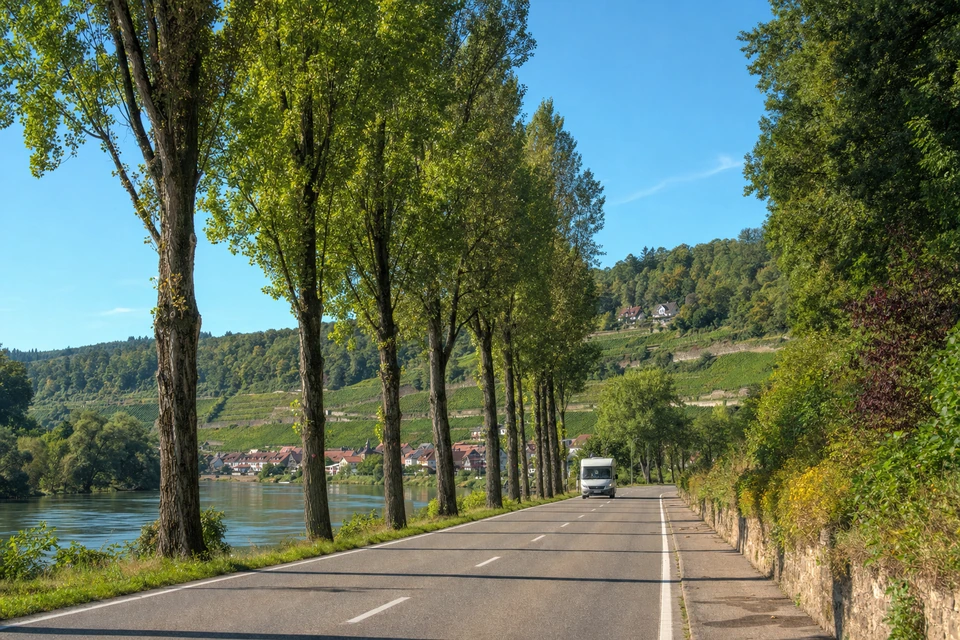 Landstraße zwischen Fluss und Waldhang in Bayern mit einem Wohnmobil in der Ferne (mit AI erstelltes Bild)
