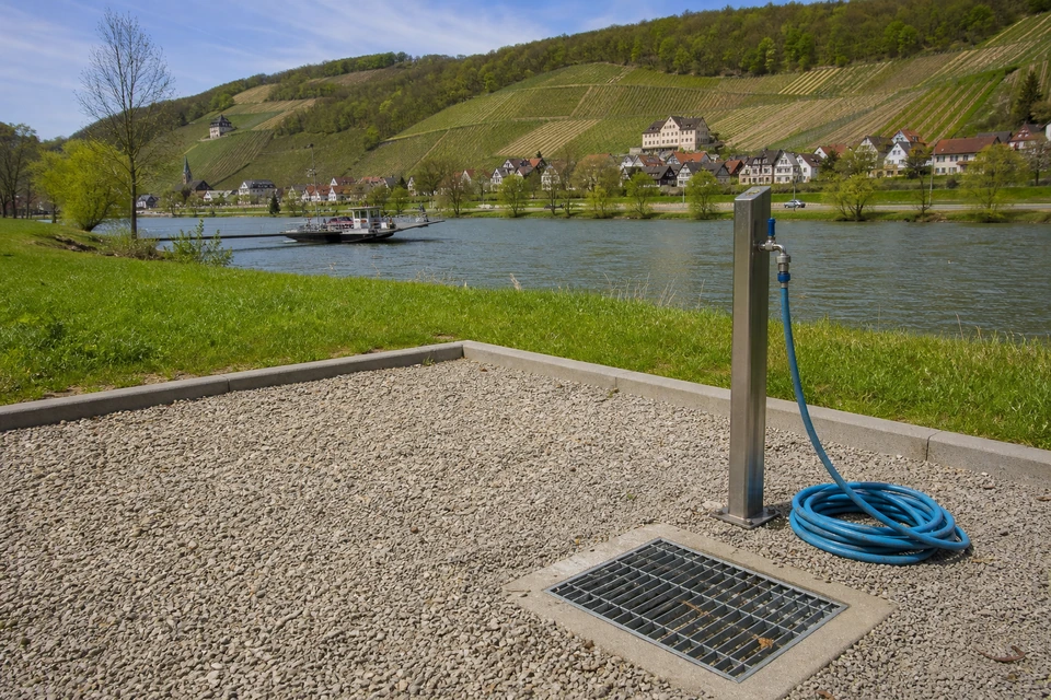 Schotterfläche mit Wasserhahn, Ablaufgitter und aufgerolltem Schlauch an einem Stellplatz (mit AI erstelltes Bild)