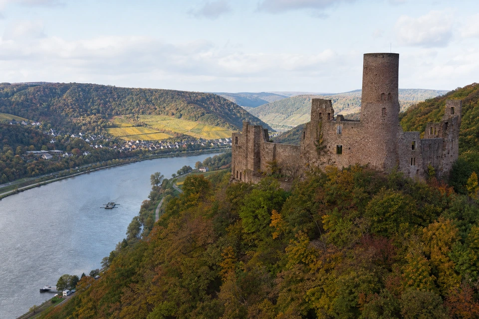 Ruine einer mittelalterlichen Höhenburg aus rotem Sandstein über bewaldeten Hängen (mit AI erstelltes Bild)