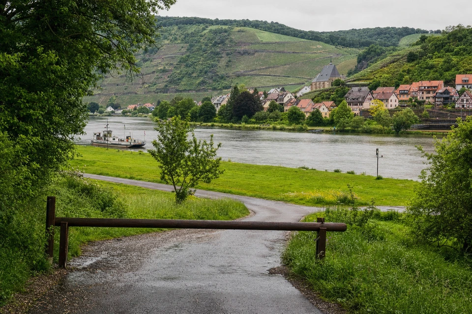 Schmale Zufahrtsstraße, die zu einer Wiesenparzelle am Fluss abbiegt, nach Regen (mit AI erstelltes Bild)